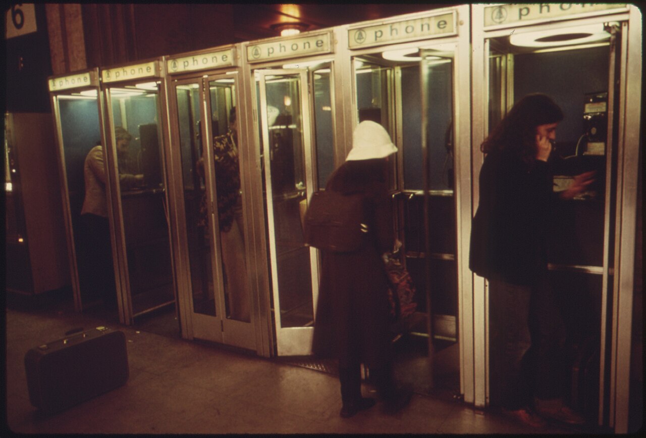 Passageiros usando telefones públicos em estação de trem, 1974