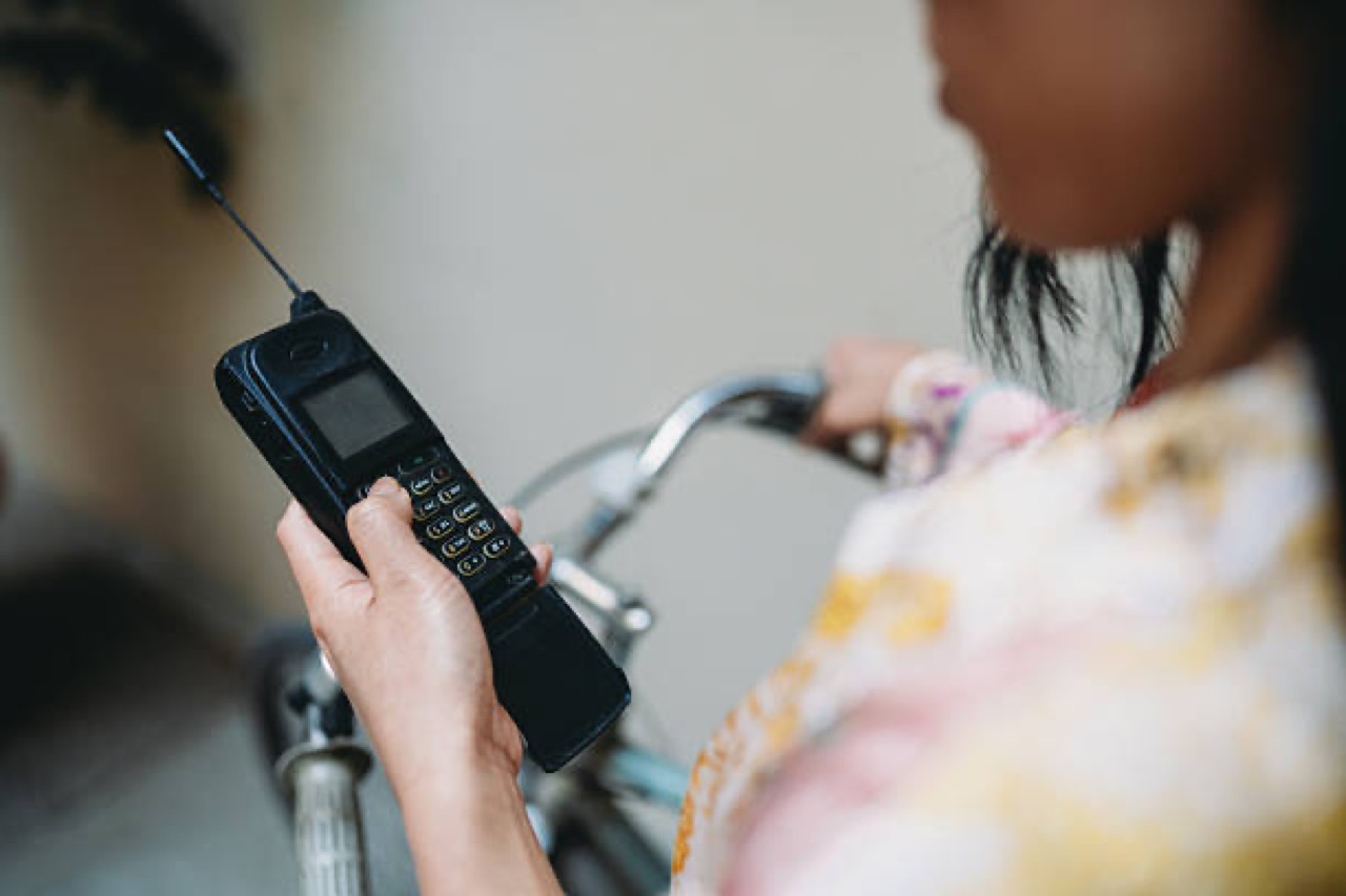 Mulher discando num celular tijolão de antena enquanto anda de bicicleta