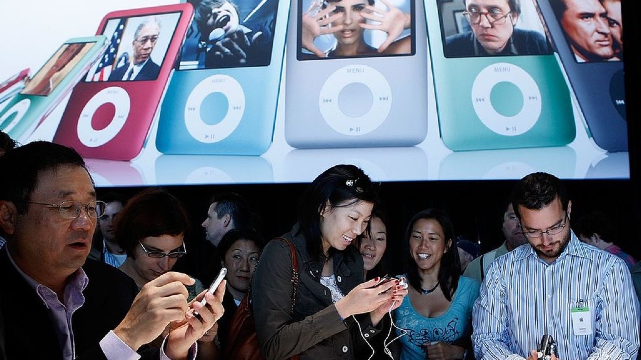 Lançamento do iPod Nano — tela grande exibindo os modelos, pessoas testando os aparelhos com fones de ouvido em primeiro plano