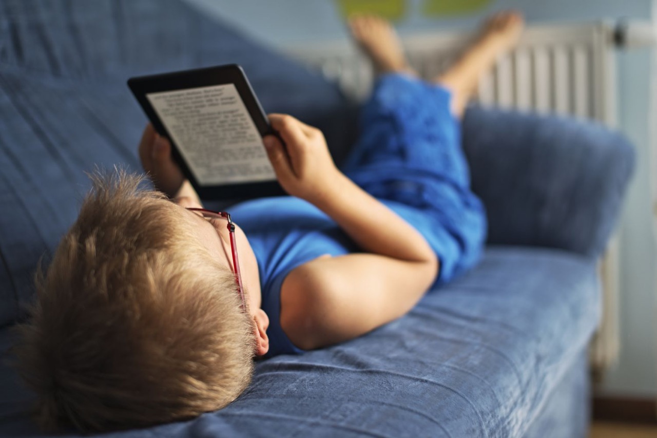 Criança de óculos deitada no sofá, lendo num Kindle