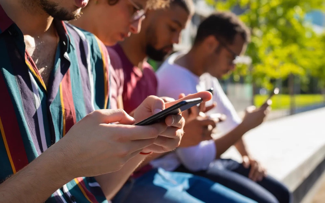 Fila de rapazes sentados lado a lado, cada um no próprio smartphone, sem interagir entre si