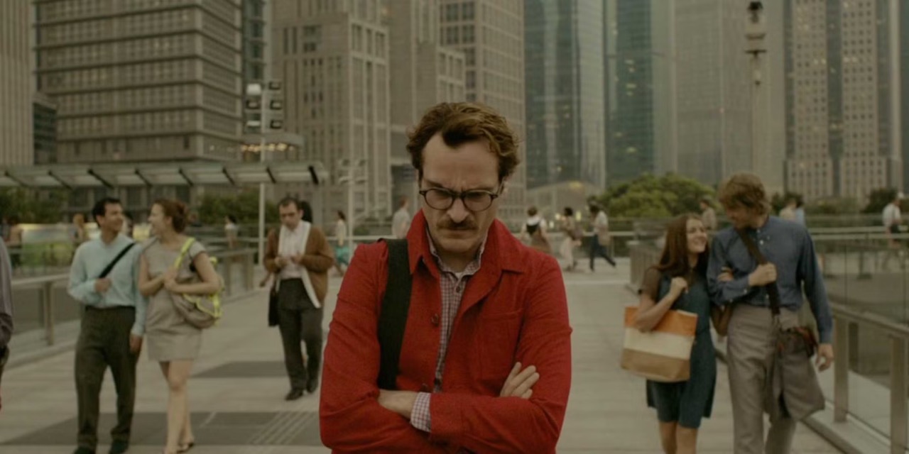 Still do filme Her — Theodore parado, de braços cruzados, no meio de uma praça cheia de gente andando em pares ao seu redor