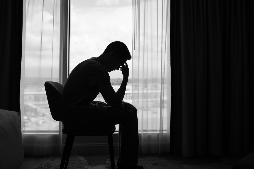 Silhueta de homem sentado, cabeça apoiada na mão, olhando pela janela